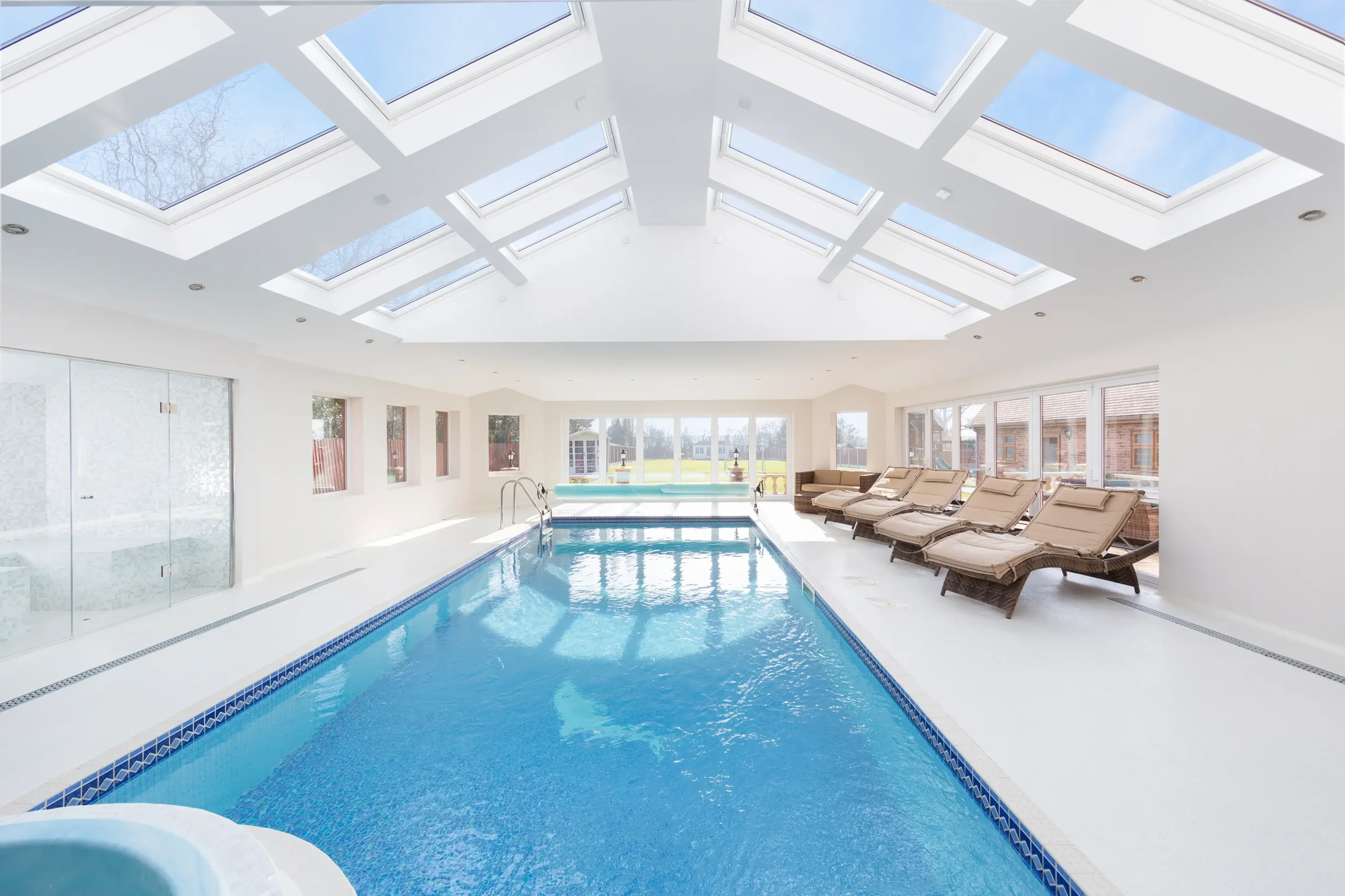 Indoor swimming pool with skylights and poolside loungers.