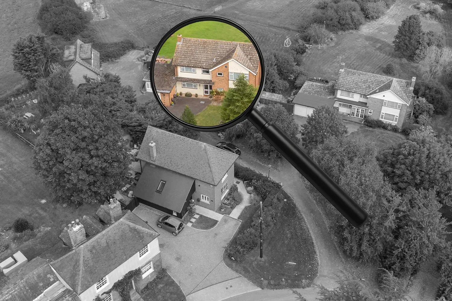A magnifying glass highlighting a single house in colour within a black and white aerial view of a residential area.